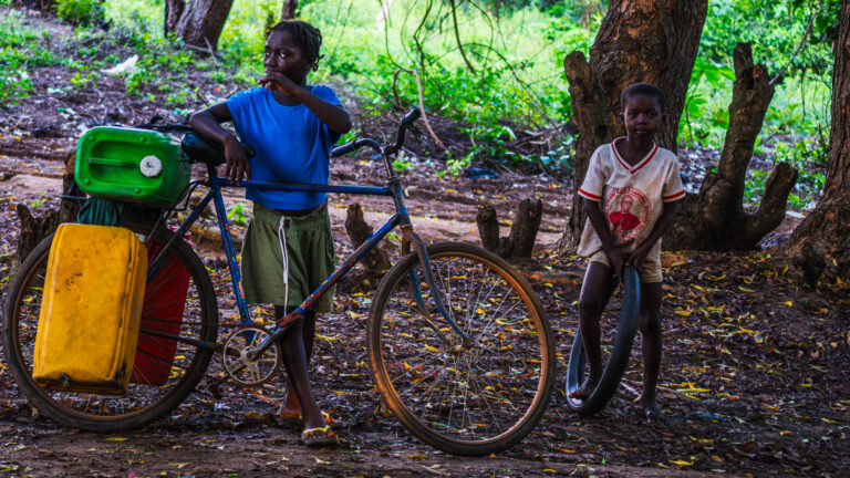 Trois enfants et un vélo chargé sous des arbres dorés à Abidjan, photo documentaire de Ka.O